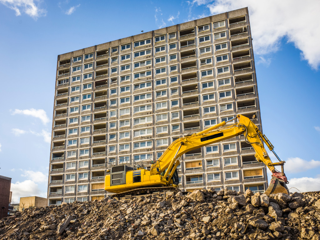 yellow excavator digging on a mound of rubbish in front of a unfinished building