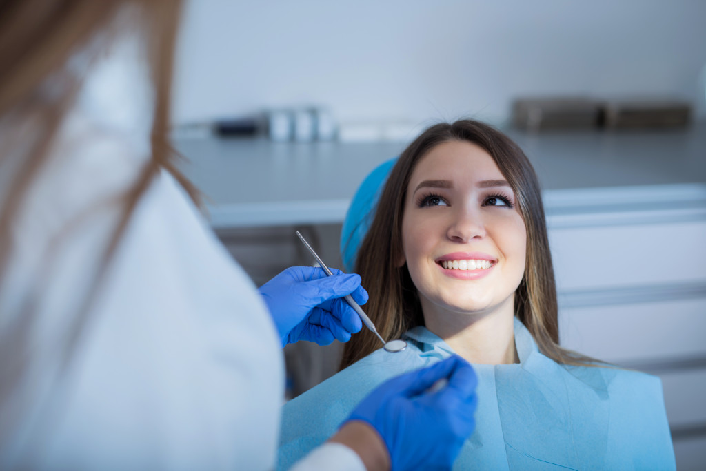 A woman wearing a big smiles while her dentist holds up a dental mirror near her mouth