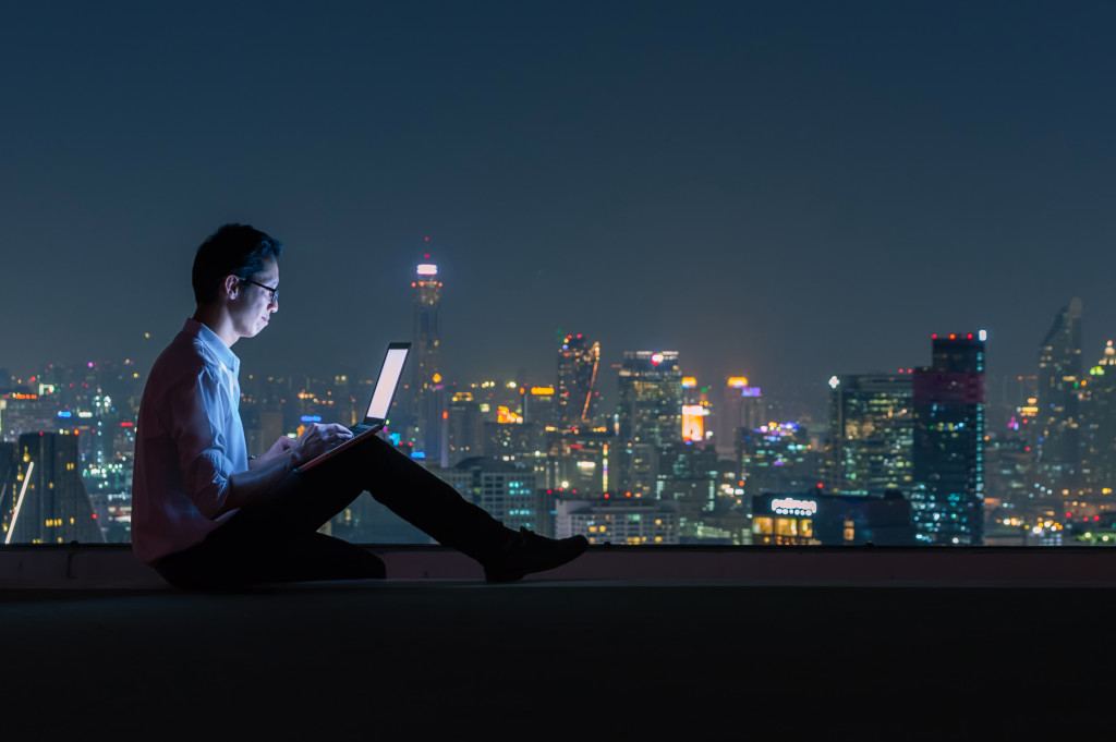 A man on a rooftop using his laptop at night