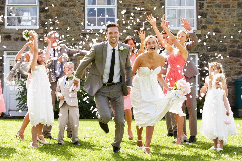 wedding couple running happily while people at the back sprinkled flower petals on them