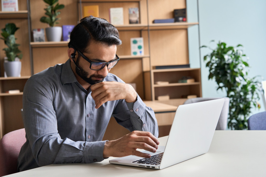 man with glasses using laptop to manage remote startup in home office