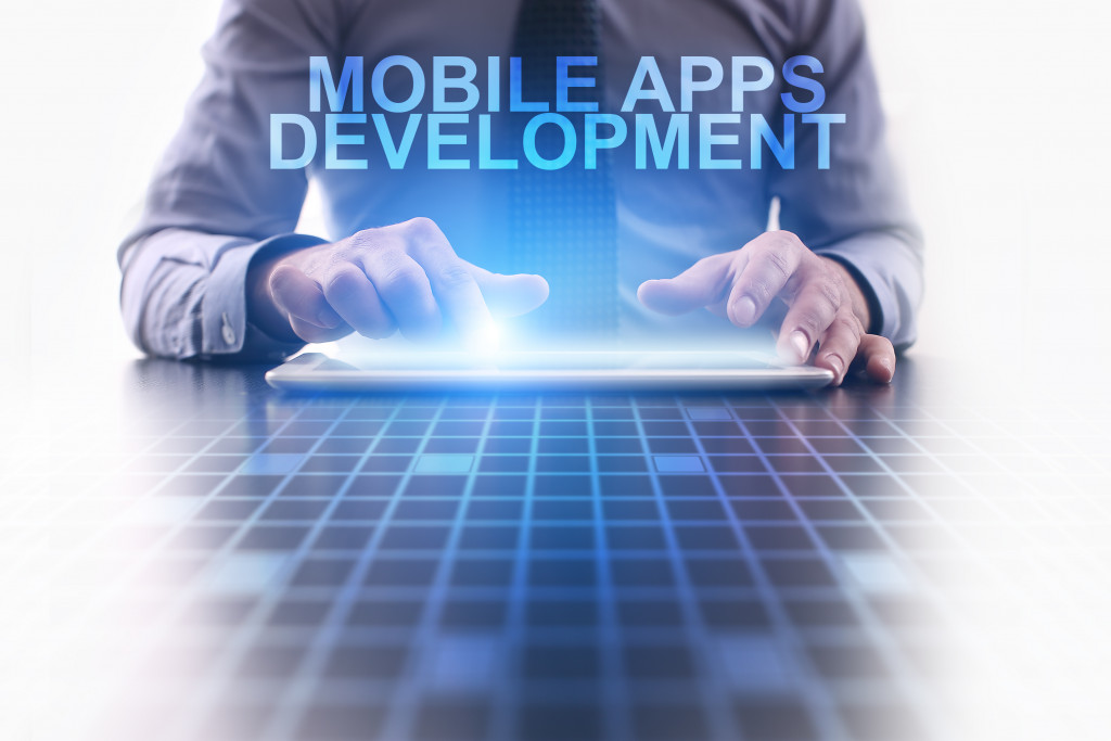 MOBILE APPS DEVELOPMENT words with a businessman working on his tablet in the background